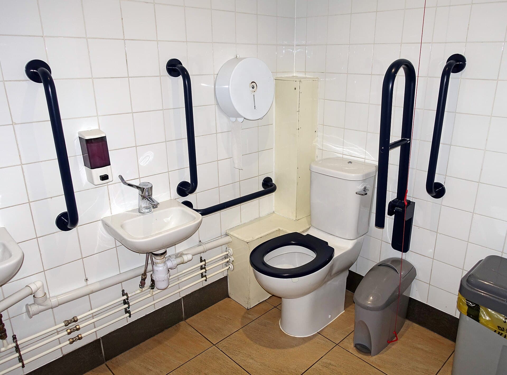An accessible toilet cubicle with grab rails and a raised pan