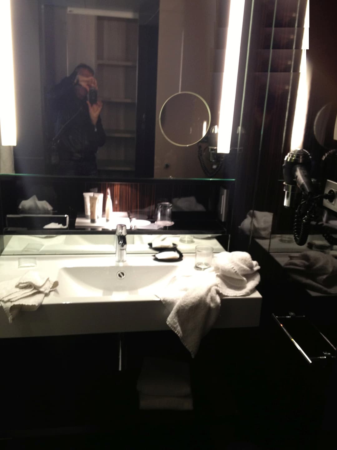 A hotel bathroom with a mirror, basin and toilet in warm light