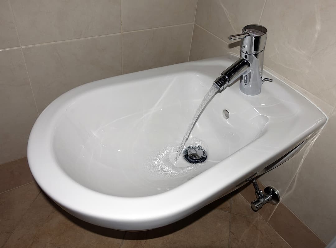A traditional ceramic bidet fixture beside a toilet in a tiled bathroom