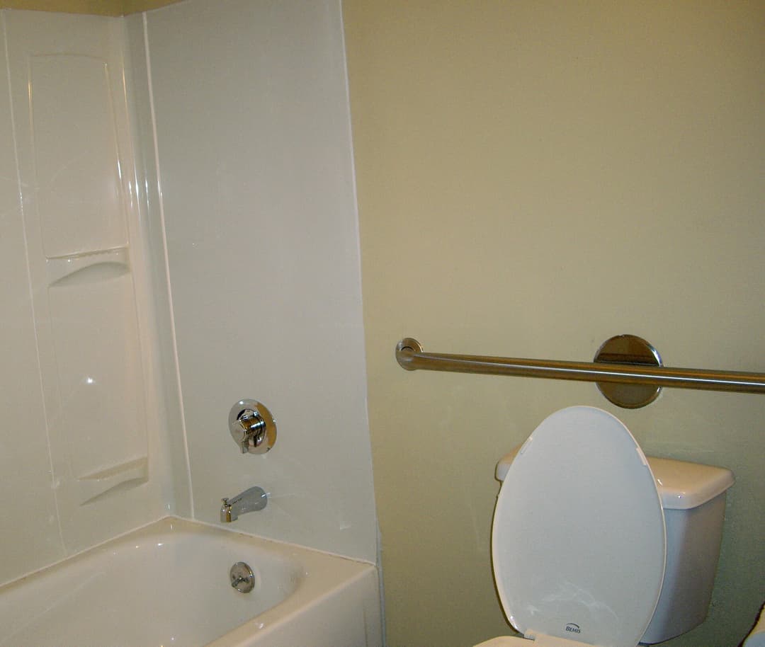 A stainless steel grab bar mounted on tiled bathroom walls