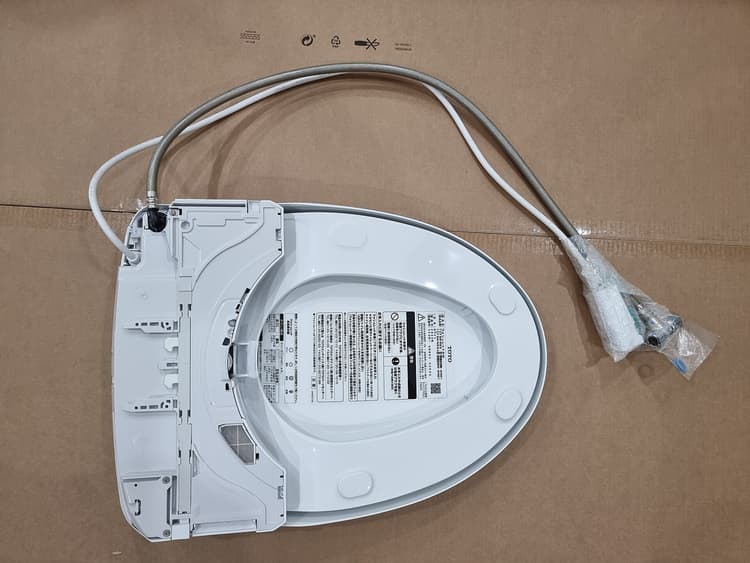 Underside of an electronic bidet seat showing the retractable wash nozzle