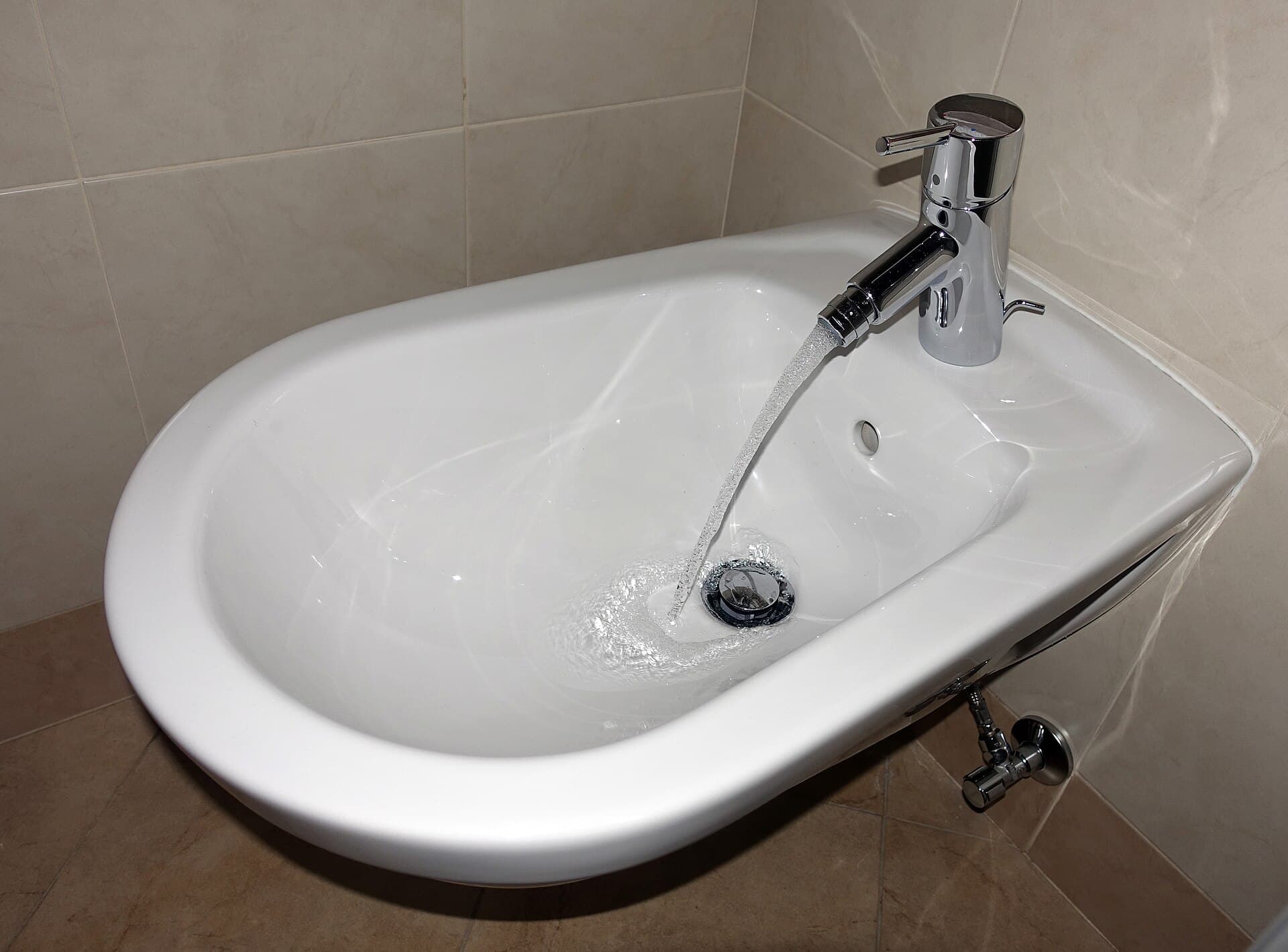 A traditional ceramic bidet fixture beside a toilet in a tiled bathroom